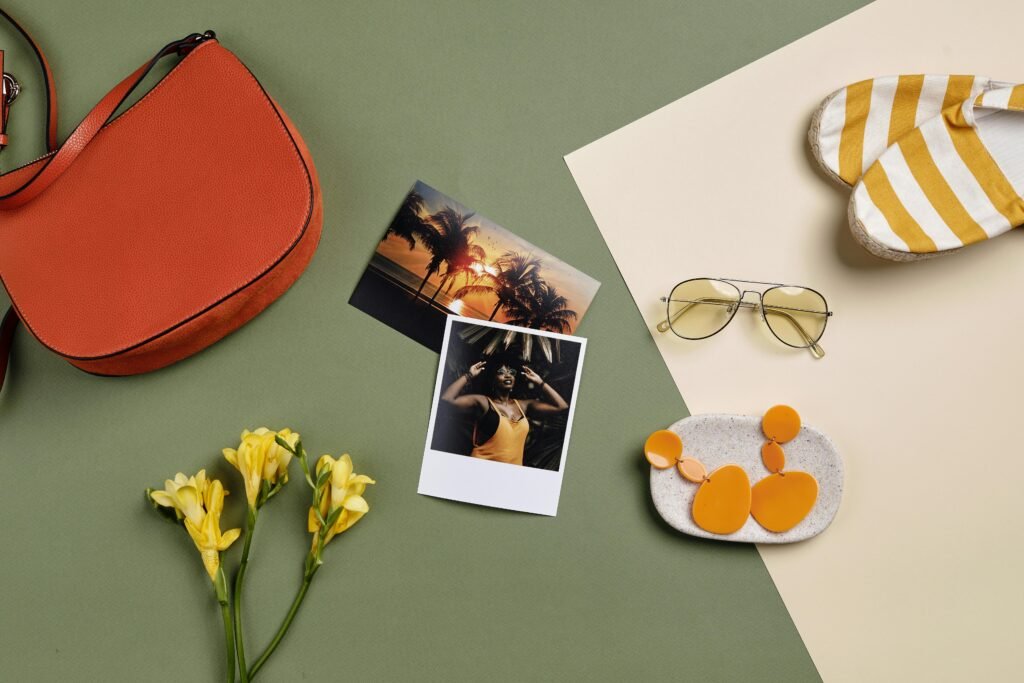 Stylish summer accessories and polaroid photos arranged on a green background.